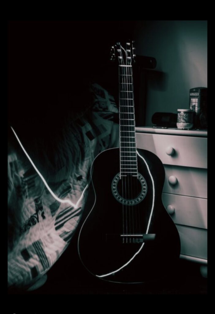 Akustikgitarre lehnt im schummrigen Zimmerlicht am Bett